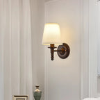 Lit Clérachic wall light with a straight arm and white fabric shade, on a pale wall beside a sheer curtain and a small green vase.
