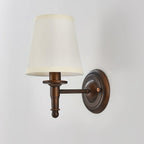 Unlit Clérachic wall light on a grey wall, a wide cream shade over a straight brown arm with a ribbed column and ball end.