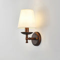 Clérachic wall light with a short brown arm and a dish below a glowing white shade, a soft warm halo on a grey wall.