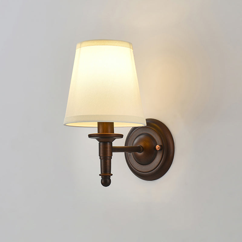 Lit Clérachic wall light with a straight arm and a wide white shade, warm light falling on a pale grey wall.