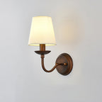 Clérachic wall light with a shallow dish and a curved arm, its white shade lit on a pale grey wall.