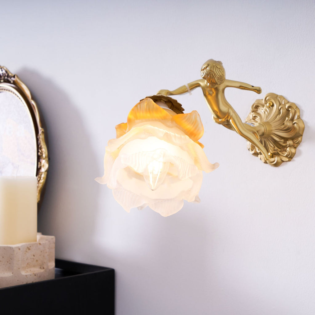 Closer view of the Clérachic cherub wall light, its frosted rose shade lit warm above a candle on a black cabinet.