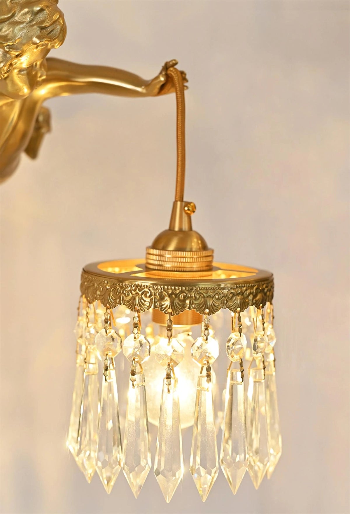 Close view of the lit crystal-fringed shade and brass cap, hung from the cherub's hand on this Clérachic wall light.