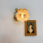 A Clérachic wall light with a lit rose-shaped glass shade hangs on a pale wall beside a small framed portrait.