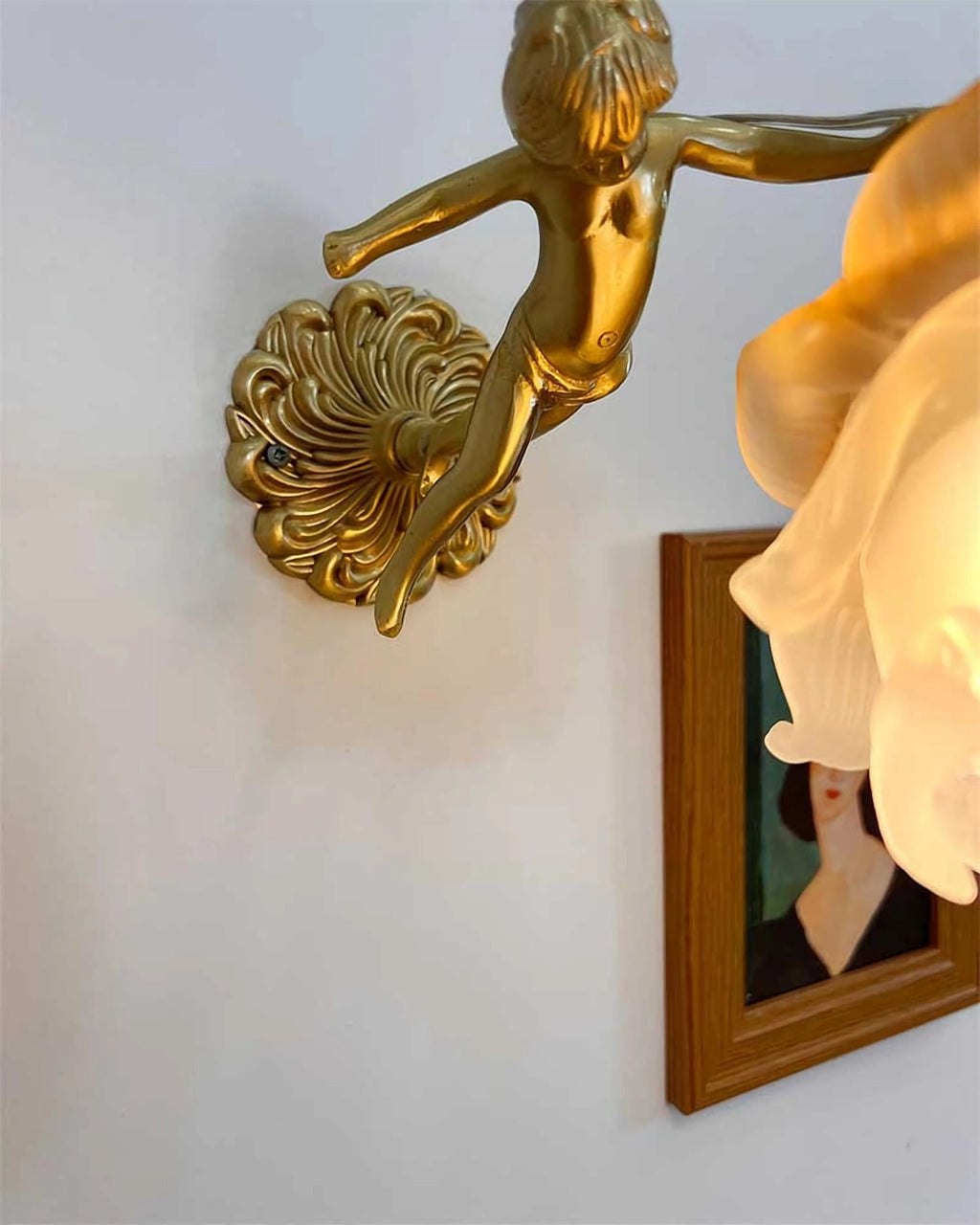 Close crop of the cherub's body and scrolled back plate on this Clérachic wall light, with the glass rose shade at the edge of the frame.