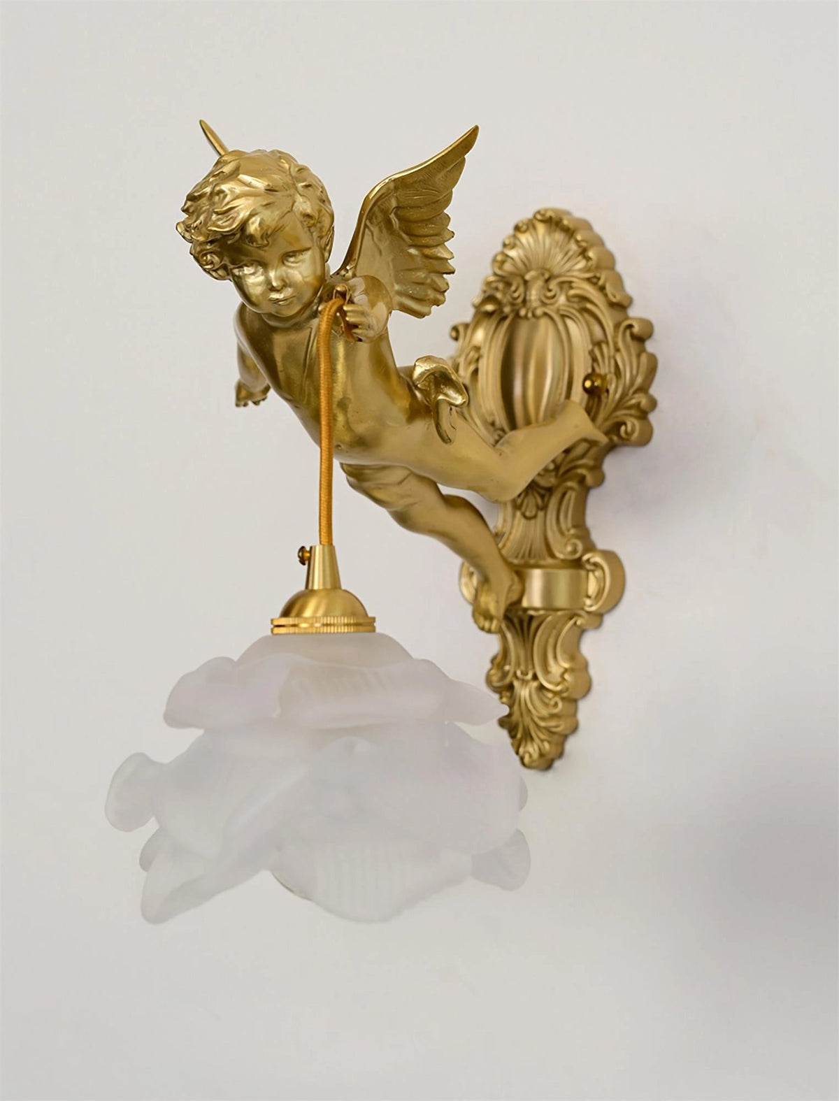 A Clérachic cherub wall light with a frosted rose glass shade and a scrolled brass back plate, on a pale grey backdrop.