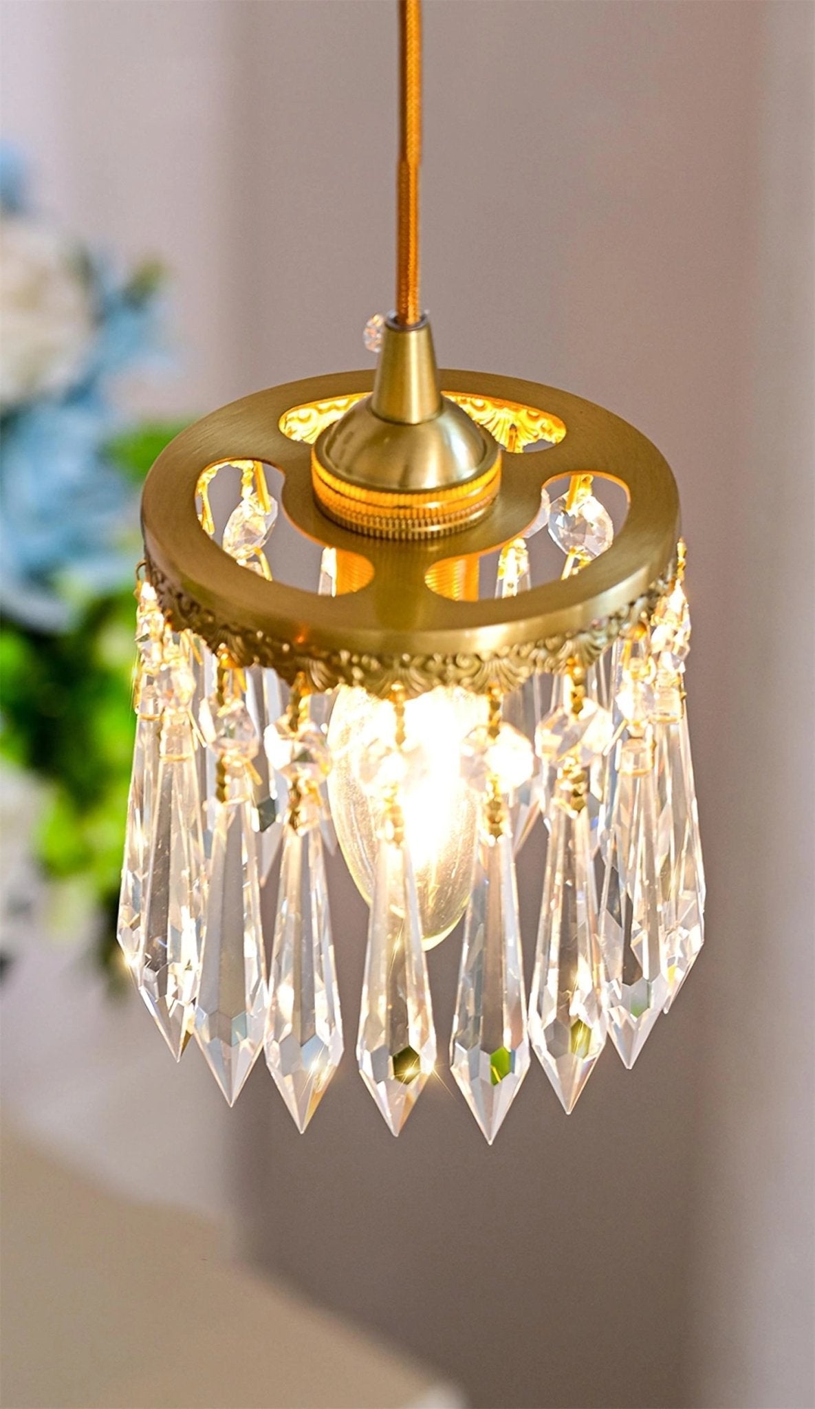 Close view of the crystal prisms and pierced brass rim of the shade on this Clérachic wall light, lit against a soft grey wall.