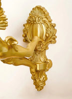 Close view of the scrolled, shell-topped back plate and the cherub's arm on this Clérachic wall light, in a gold-toned finish.