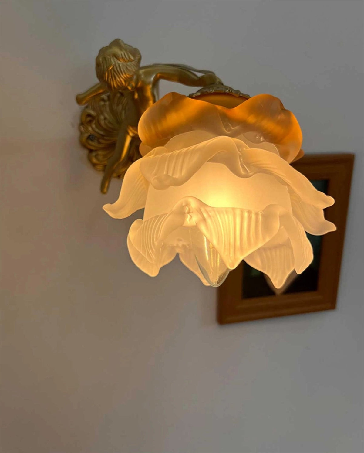 Warm light glows through the frosted petals of the rose shade on this Clérachic wall light, with a portrait frame behind.