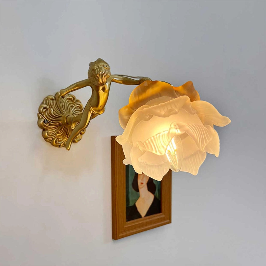 Side-on, a Clérachic cherub wall light with a lit rose shade projects from its round back plate above a framed portrait.