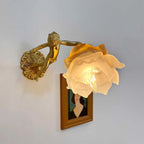 Side-on, a Clérachic cherub wall light with a lit rose shade projects from its round back plate above a framed portrait.