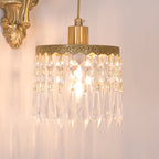 Close view of the lit crystal-fringed shade on this Clérachic wall light, with the glow spilling warm onto a pale wall.