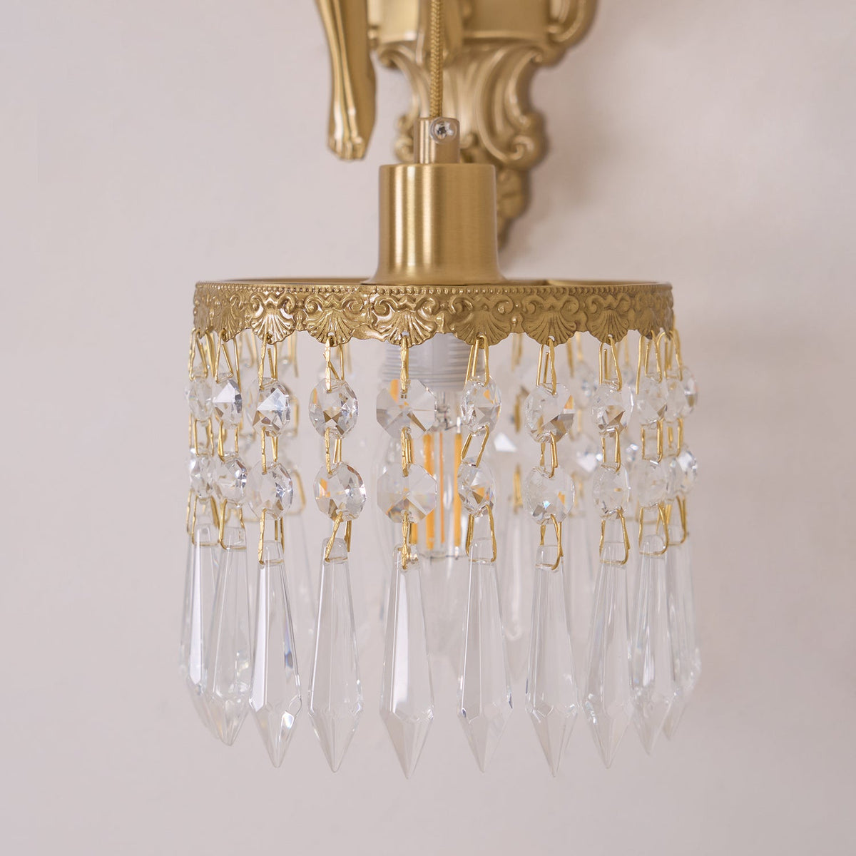 Unlit crystal drops and a pierced brass rim, in close view, on the shade of this Clérachic wall light.