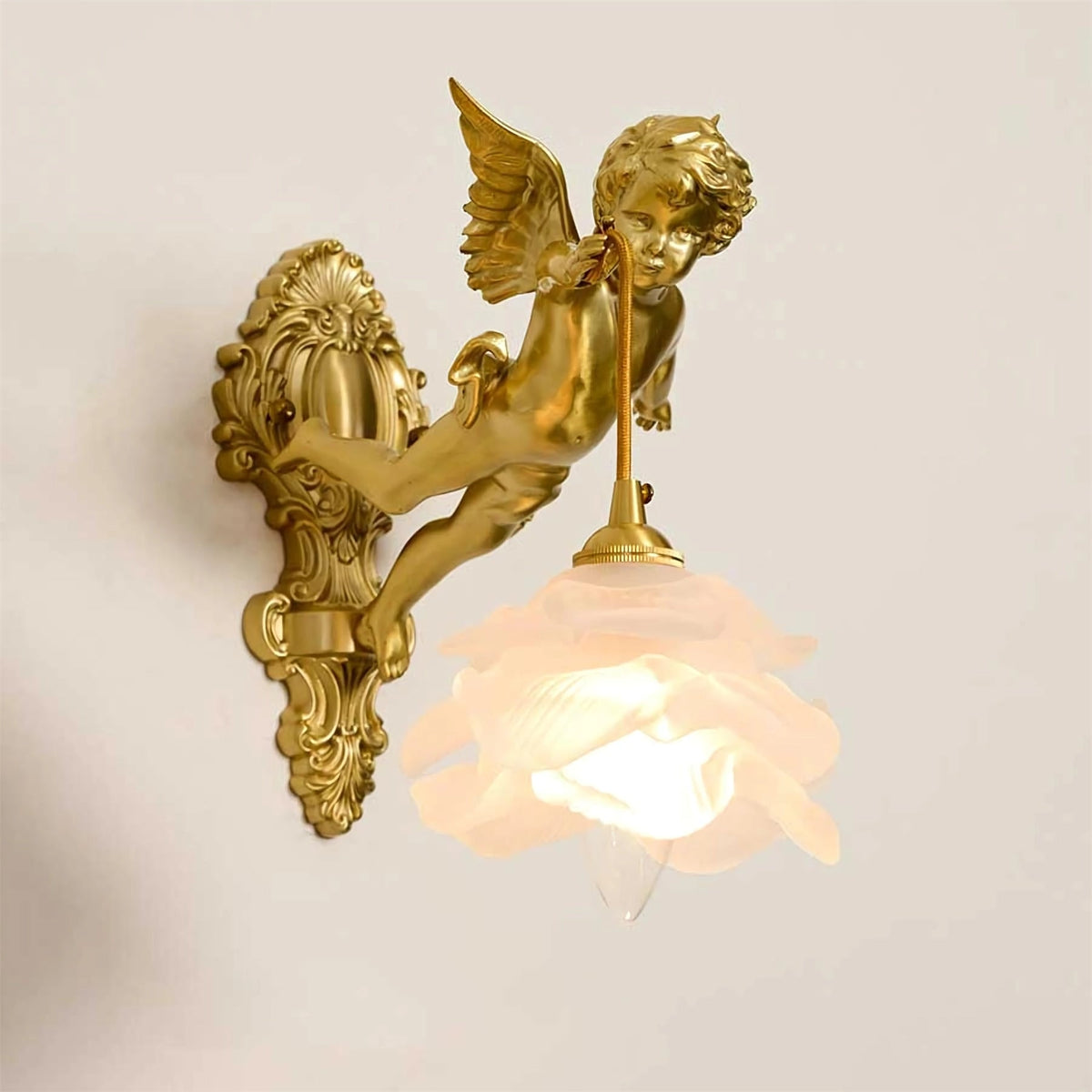 A Clérachic cherub wall light with a lit frosted rose shade and a long scrolled back plate, on a soft beige backdrop.