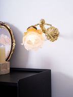 The small cherub and round back plate of this Clérachic wall light, with its rose shade lit above a black cabinet.