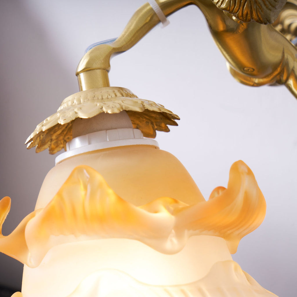 Close view of the brass cap, bulb holder and amber-edged rose shade on this Clérachic wall light, with the cherub's arm above.