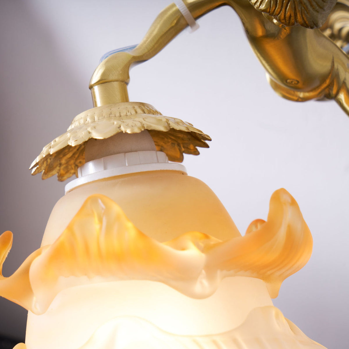 Close view of the brass cap, bulb holder and amber-edged rose shade on this Clérachic wall light, with the cherub's arm above.