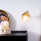 Wide view of a Clérachic wall light with a rose shade on a white wall, above a black cabinet with candles and a framed print.
