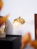 Through soft autumn-leaf blur, a Clérachic cherub wall light glows on a white wall above a black cabinet.