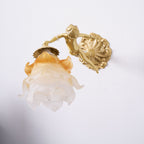 Seen from the side, the amber-tipped rose shade and brass back plate of this Clérachic cherub wall light stand out from a white wall.