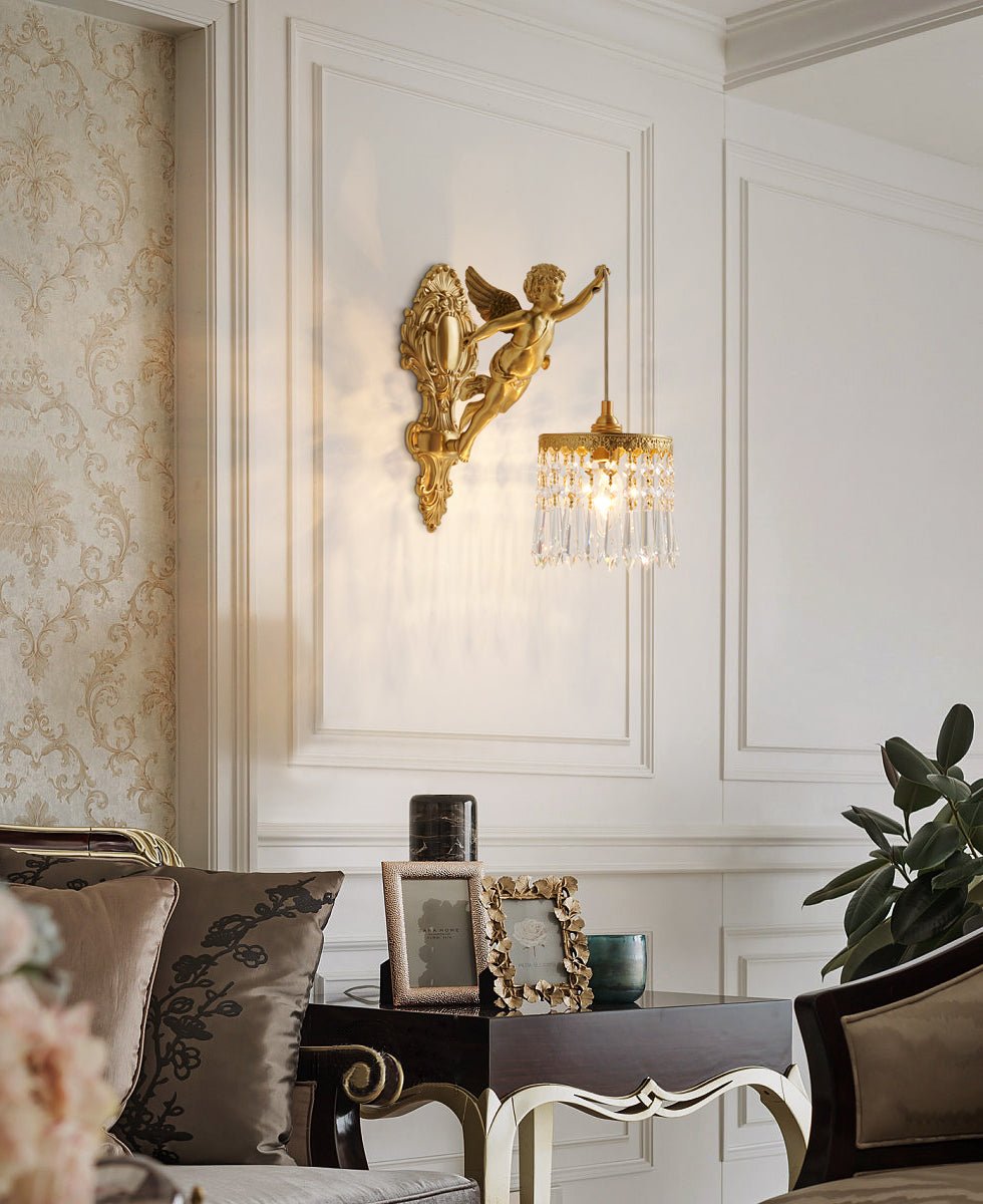 A Clérachic cherub wall light on a panelled white wall above a dark side table with picture frames and a green plant.