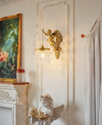 Next to a gilt-framed landscape painting, a Clérachic cherub wall light hangs on a panelled wall above a mantel and a small angel figure.