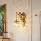 Nearer view of a Clérachic cherub wall light on a panelled wall, with a gilt-framed painting and a red-lidded glass jar below.