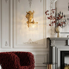Closer view of a Clérachic cherub wall light above a grey fireplace, with a red woven armchair and a vase of dark branches.