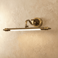 Clérachic antique brass wall light with a fluted bar and scrolled arm, lit with a warm glow against a limewashed plaster wall.