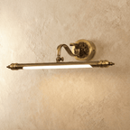 Clérachic antique brass wall light with a fluted bar and scrolled arm, lit with a warm glow against a limewashed plaster wall.