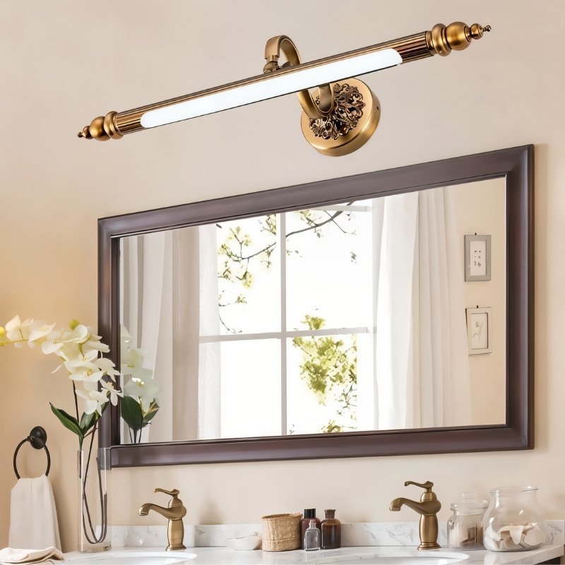 Clérachic antique brass bar light above a dark framed vanity mirror, with brass taps, white flowers and a towel ring below.