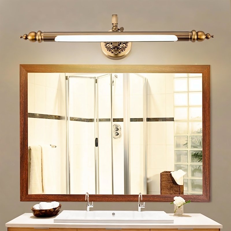Clérachic antique brass bar light centred over a wood-framed mirror above a white double vanity basin in a bathroom.