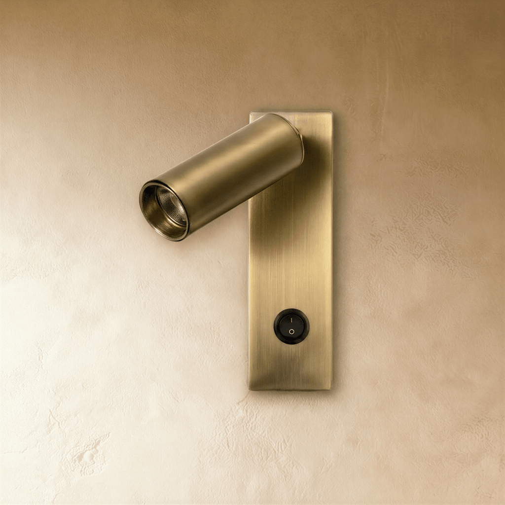 Clérachic brushed brass wall reading light, switched off, with a tilted cylinder head and a black rocker switch on the plate.