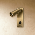 Clérachic brushed brass wall reading light, switched off, with a tilted cylinder head and a black rocker switch on the plate.