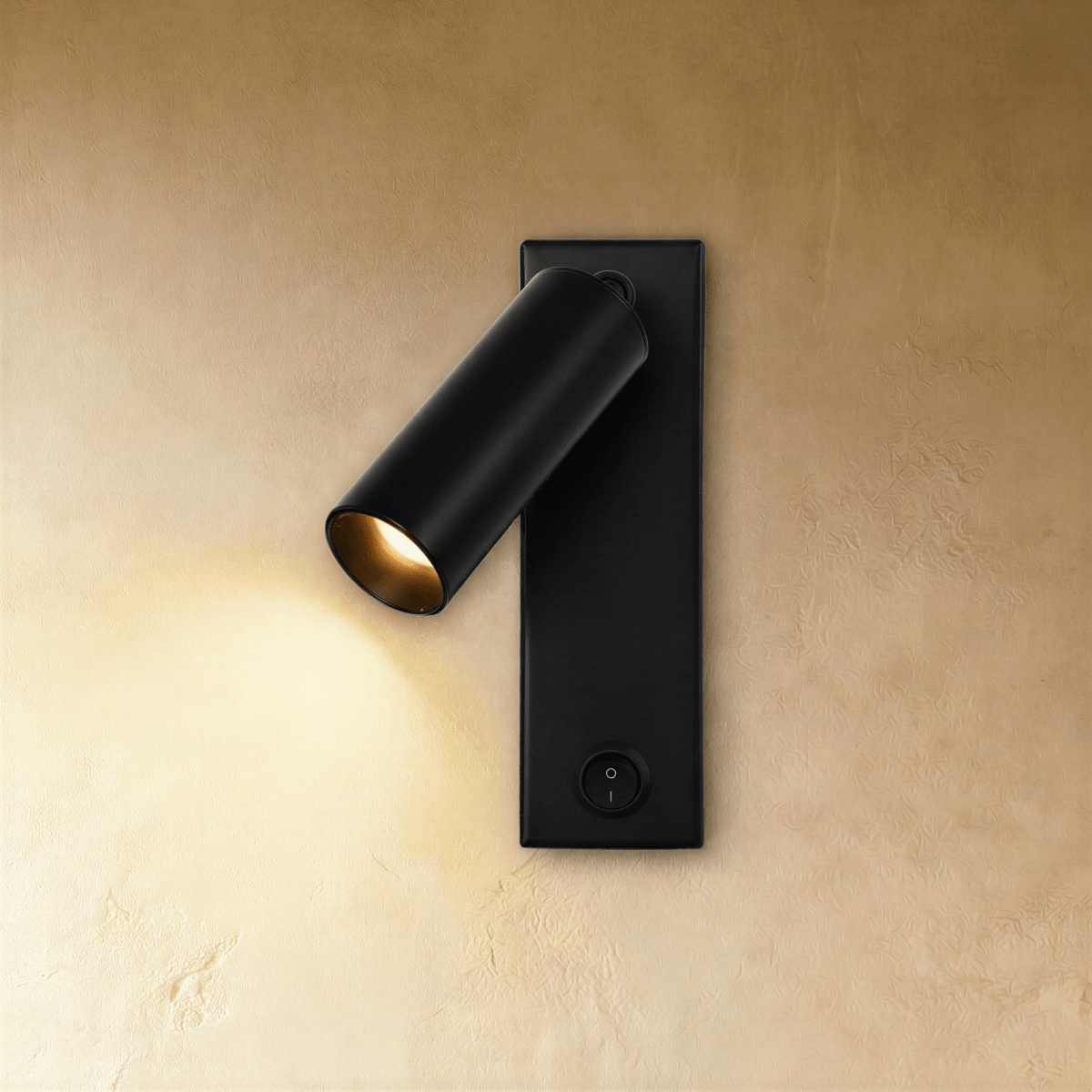 Clérachic matt black wall reading light with a tilted cylindrical head casting warm light, black rocker switch on the plate.