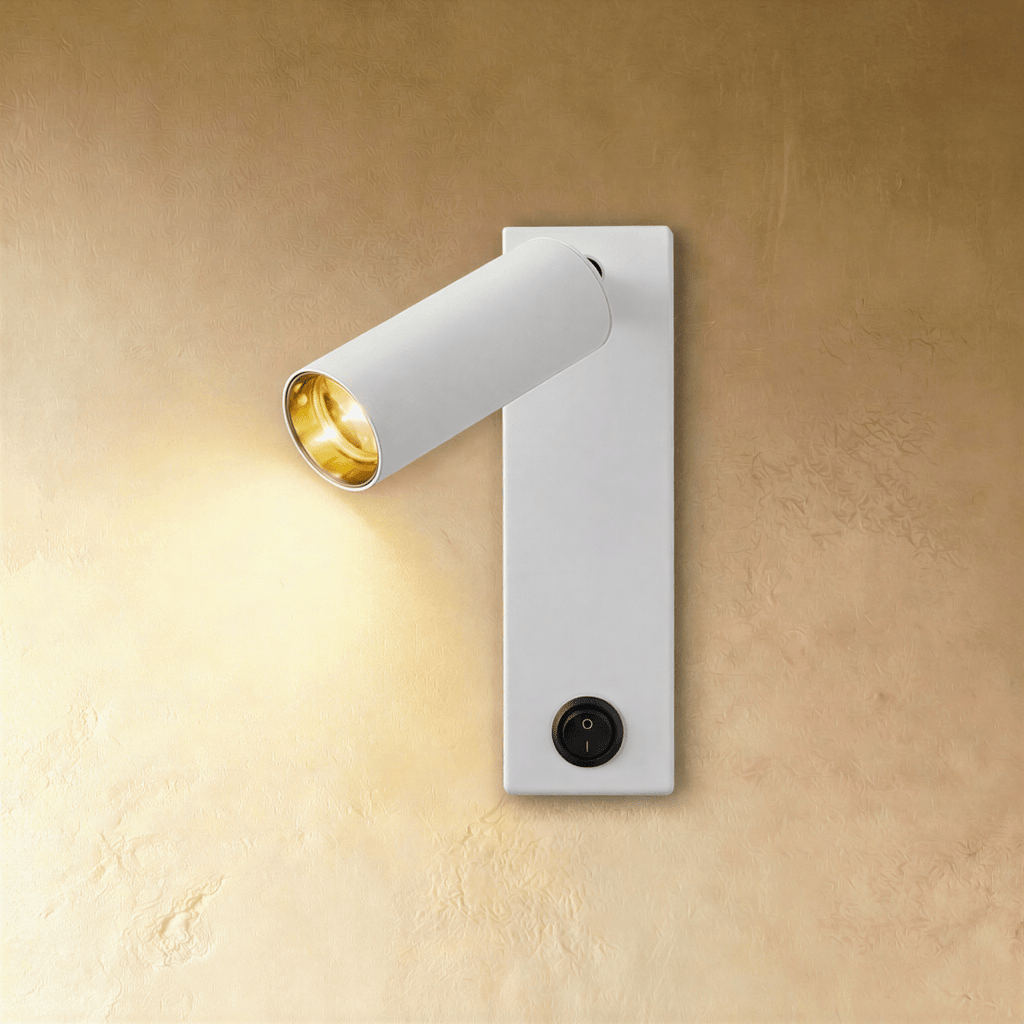 Clérachic white wall reading light with an angled cylinder head, gold-toned inner reflector lit warm and a black rocker switch.