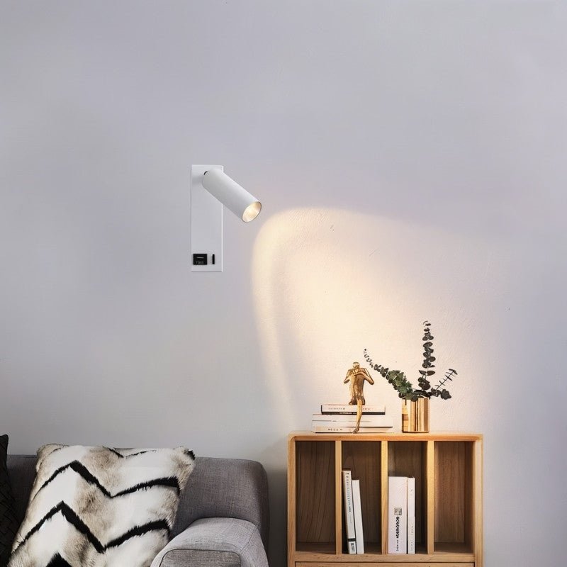 Clérachic white wall reading light with a USB port, throwing a warm pool of light over a wooden shelf and a gold figurine.