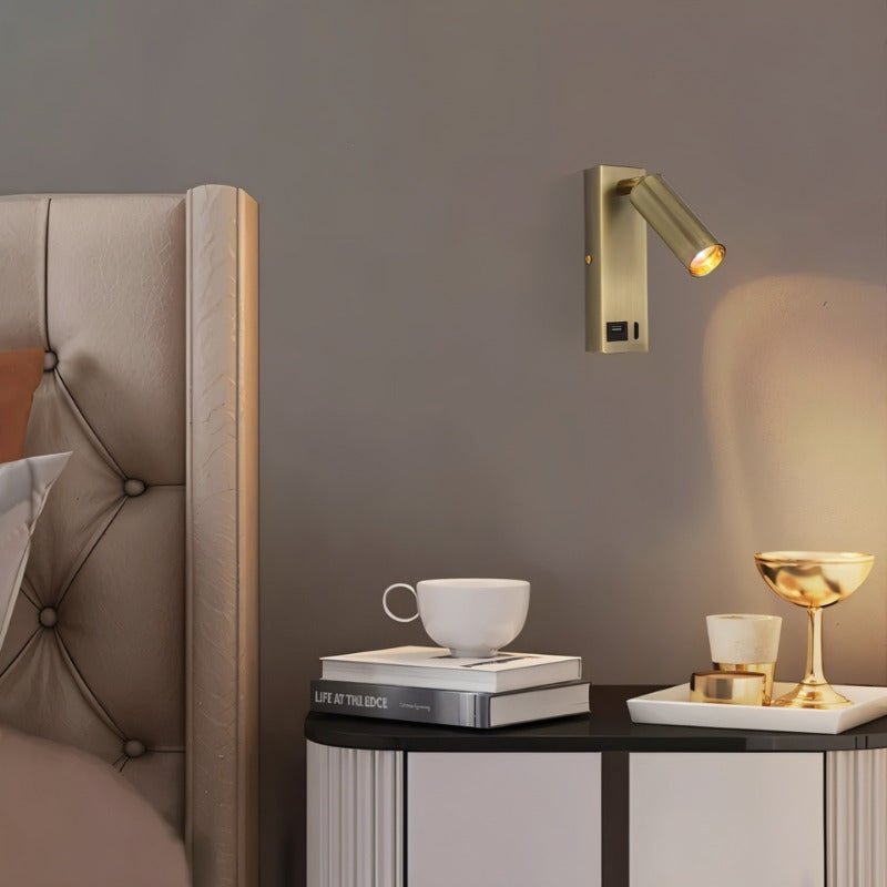 Clérachic brass wall reading light with a USB port beside a tufted headboard, lighting a bedside table with books and a gold goblet.