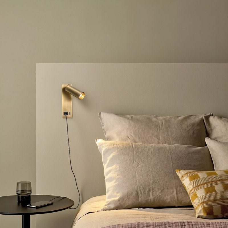 Clérachic brass wall reading light with a USB cable running down to a phone on a round bedside table, over a linen-dressed bed.