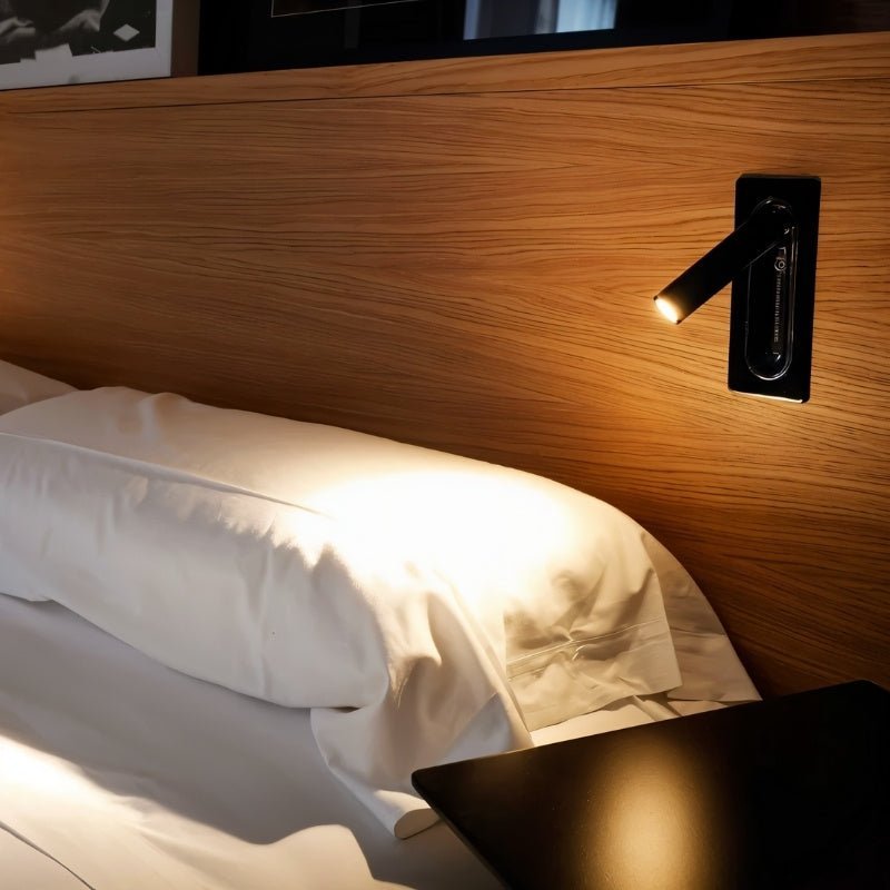 Clérachic black wall reading light on an oak headboard, its spotlight pooling warm light on a white pillow.