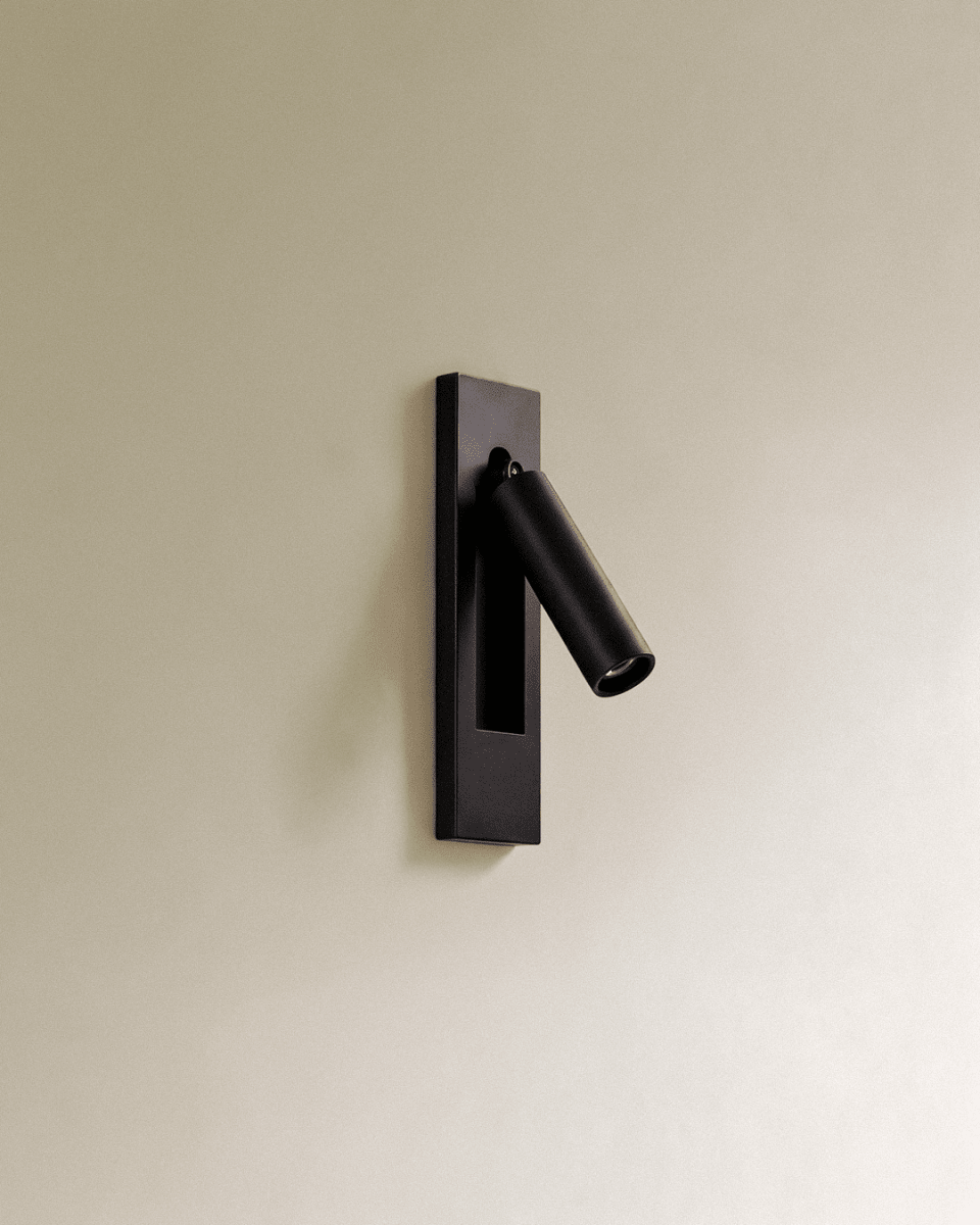 Clérachic black recessed wall reading lamp with a slim cylindrical head swung out from a rectangular plate on a cream wall.
