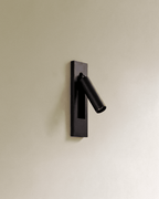 Clérachic black recessed wall reading lamp with a slim cylindrical head swung out from a rectangular plate on a cream wall.