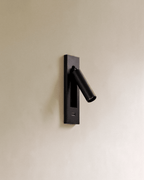 Clérachic black wall reading lamp with a USB-C port in the lower plate and an angled cylindrical head on a cream wall.