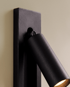 Close view of a Clérachic black wall reading lamp: textured matte plate, small pivot screw and the round lamp head with warm glow.