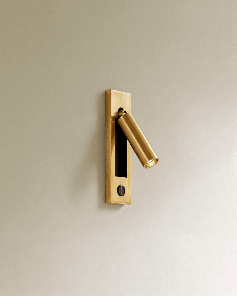Clérachic all-gold wall reading lamp with a round dark push button in the lower plate and an angled cylindrical head.