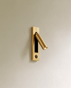 Clérachic all-gold wall reading lamp with a round dark push button in the lower plate and an angled cylindrical head.