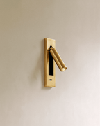 Clérachic all-gold wall reading lamp with a USB-C port in the lower plate and an angled cylindrical head on a soft taupe wall.
