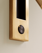 Close view of the brushed gold plate on a Clérachic wall reading lamp, with a dark metal round push button below the recess.