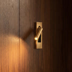 Close view of a Clérachic all-gold wall reading lamp throwing a warm beam across walnut wood panelling.