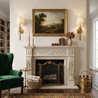 A pair of Clérachic wall lights with pleated shades flank a gilt-framed landscape painting above a carved white fireplace.